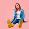 Cheerful girl sitting on the floor. she`s wearing a blue coat and yellow rubber boots. joyful laughter and enthusiastic expression