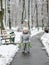 A cheerful girl in warm silver overalls is standing on the path in winter