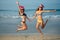 Cheerful girlfriends in a santa hat and bikini jumping on the beach