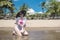 A cheerful and glamorous asian lady kneeling on the sand by the shore. At a tropical resort and beach