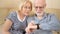Cheerful good-looking senior couple sitting on sofa at home. Using smartwatch, browsing, reading