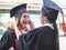 Cheerful  graduated women in graduation gowns, helping each other dress up, smiling happily. . Education, successful and