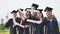 Cheerful graduates pose with raised diplomas on a sunny day.