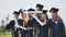 Cheerful graduates pose with raised diplomas on a sunny day.