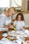 Cheerful grandma in white apron with cute curly granddaughter spend wonderful time in the kitchen.