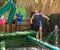 Cheerful guy balancing on soft log between swinging bags over pool with water