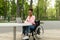 Cheerful handicapped black lady in wheelchair using laptop pc for online job at urban park, free space