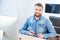 Cheerful handsome designer holding stylus and sitting in office