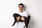 Cheerful handsome man carry black pug and smiling, staring at camera happy. Dog owner holding cute dog in arms, standing