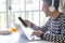 Cheerful handsome teenager using laptop at home in front of the window wearing headphones and holding smart phone. Millenial