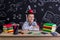 Cheerful and happy hellion schoolboy sitting at the desk with books, school supplies, with a red apple on the top of his