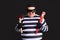 Cheerful happy thief in striped clothes standing over black background
