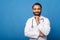 A cheerful Indian doctor with a beard poses with folded arms over his white lab coat