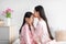 Cheerful japanese millennial female kissing at forehead of teenage girl in bedroom interior, profile, free space