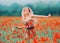 Cheerful and joyful attractive lady with blond hair in a cute tight dress, runs across the poppy field, holding a small