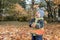 Cheerful kid catching maple leaves falling in autumn city Park