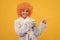 cheerful kid in fancy orange wig hair wear home bathrobe directing on copy space, promotion