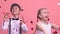 Cheerful kids jumping, playing with heart-shaped confetti on pink background