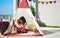 Cheerful kids are playing in teepee tent on a sunny patio