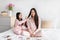 Cheerful korean teenage girl combing long smooth hair to millennial woman, sit on bed with cosmetics