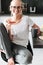 Cheerful lady in glasses sitting with bread and cup of tea in kitchen