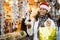 Cheerful Latina in Santa hat looking for New Year decorations in street market