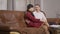 Cheerful laughing husband sitting on couch and hugging pregnant wife. Portrait of happy positive Caucasian man and woman