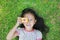 Cheerful little Asian girl takes photo with colorful digital camera lying on green lawn background