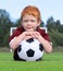 Cheerful little boy with ginger hair posing with a soccer ball. Portrait of a kid in sportswear. Little boy lying on the