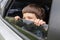 Cheerful little boy looks out the open window and enjoys ride with parents in car in summer, outdoor, free space