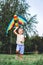 Cheerful little boy running with a multicolored kite on the city park green grass meadow. Funny childhood concept image