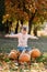 Cheerful little child girl lift very large orange pumpkin for her Halloween or Thanksgiving decoration outdoor at warm