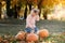 Cheerful little child girl lift very large orange pumpkin for her Halloween or Thanksgiving decoration outdoor at warm