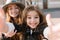 Cheerful little girl with big brown eyes making selfie standing in front of her stylish smiling mother. Elegant young