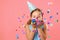 Cheerful little girl celebrates birthday. The child blows confetti from the hands. Closeup portrait on pink coral background