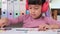 Cheerful little girl in headphones reading a book sits at the table in her room at home.