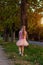 Cheerful little girl with long blonde hair in pink tulle skirt walking alone on empty street on sunset. Greeting card