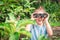 A cheerful little girl is looking through binoculars from the bushes. The child is watching the parents at a distance. The baby