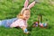 A cheerful little girl preschooler dressed in bunny ears is lying on the lawn with a basket of painted Easter eggs. Happy Easter