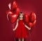 Cheerful little girl in tulle skirt holding balloons red heart on red background. Celebrating brightful carnival for kids