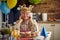 Cheerful lovely senior woman wearing inflatable golden crown and feeling joyful sitting at the table celebrating birthday