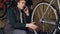 Cheerful maintenance man is talking on mobile phone while working in bike rapair workshop checking wheel spokes and