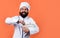 Cheerful male chef in hat with beard and moustache on orange background beating meal with beater, cuisine, copy space