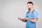 Cheerful male doctor in blue using tablet for online consult, grey background