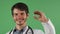 Cheerful male doctor smiling holding blue pill on green background