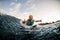 cheerful male wakesurfer lying on board rides down wave and show hands gestures and winks