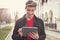 Cheerful man in jacket standing outdoors and surfing tablet happily