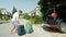 Cheerful man picking up a suitcase to pack it into his SUV in the sunny driveway