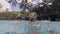 Cheerful man splashing water in outdoor swimming pool in resort hotel. Waterline view happy man having fun in swimming