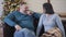 Cheerful man and woman laughing out loud as sitting at the background of Christmas tree at home. Portrait of joyful